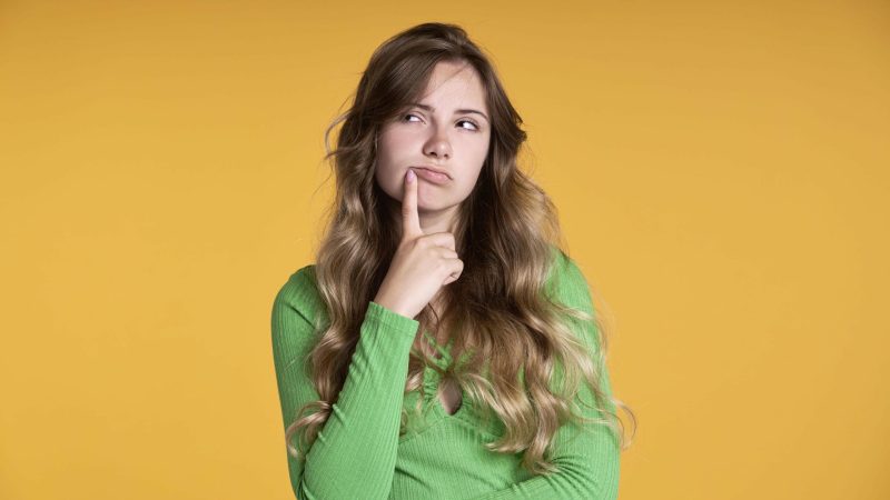 Thoughtful caucasian teenage girl on yellow background